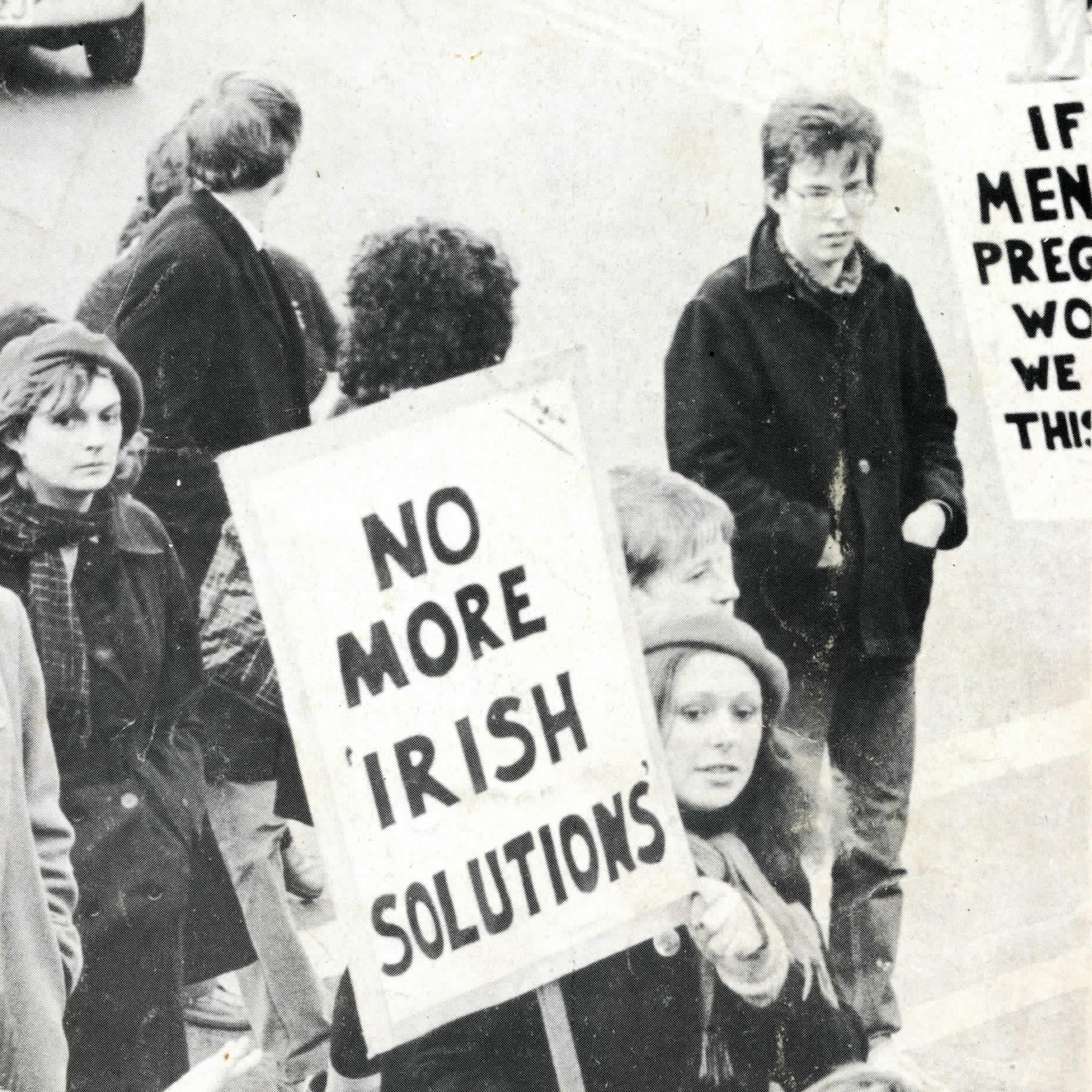 A group of protestors at a rally. A woman in the foreground holds a placard reading "No More Irish Solutions". (Image from Gralton, No. 9).