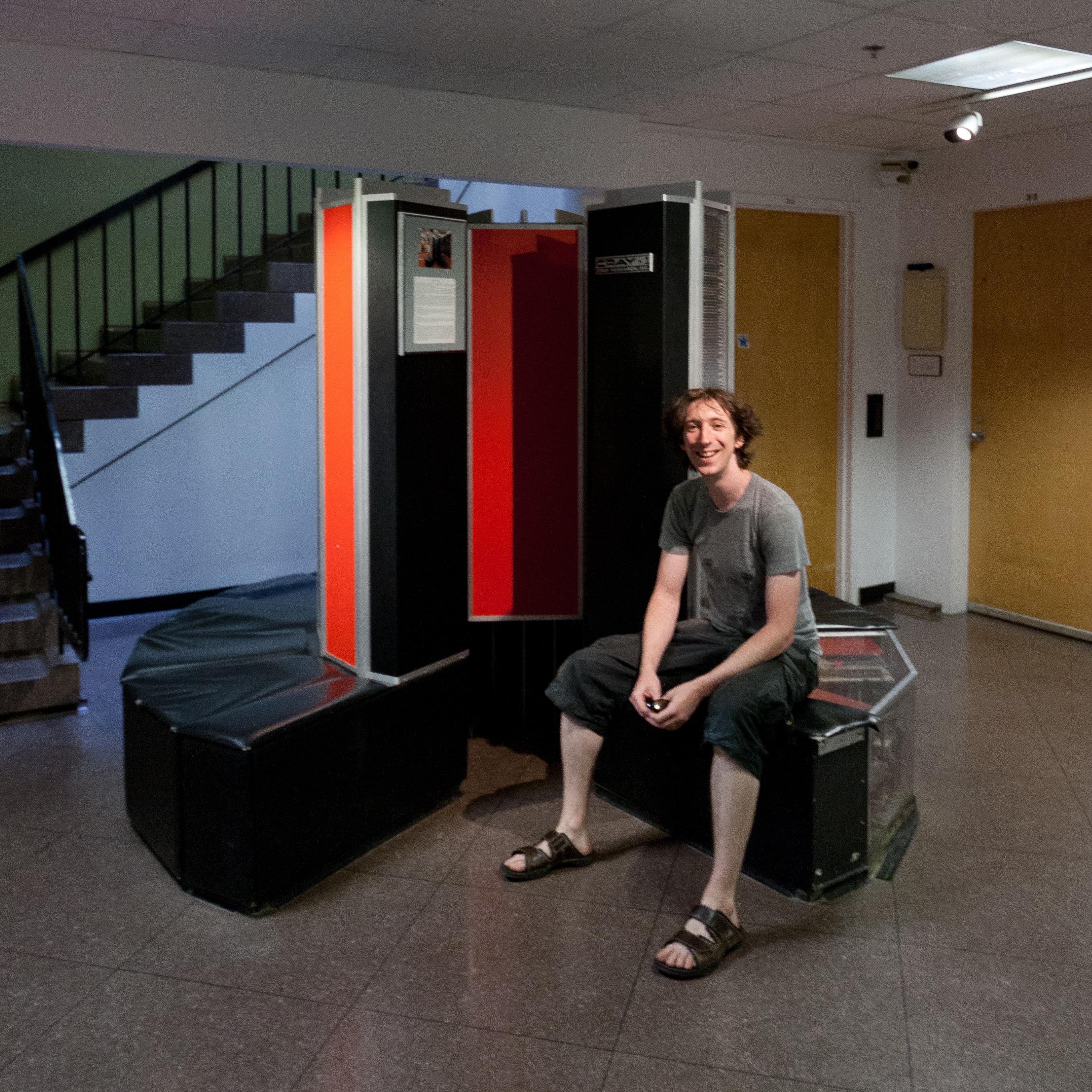 A hallway with a weird sort of c-shaped leather bench in it. Dave is sat on it looking very happy. Because it’s not just seat! No, this is a Cray-1 supercomputer! In fact, it’s the first one that was ever ordered!
