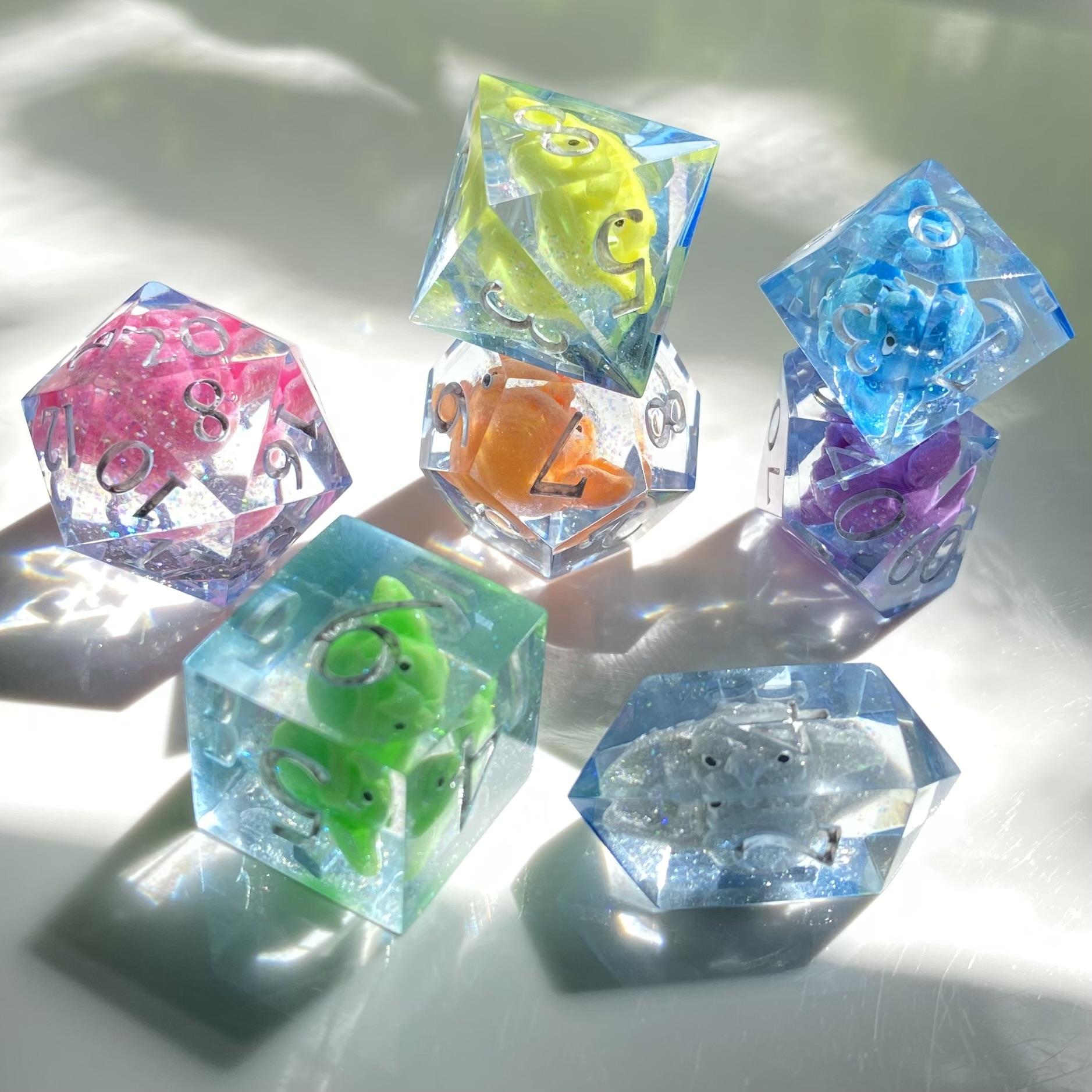 Angry goblin heads in a rainbow of neon colors grimace inside each die of a seven piece gaming set. They also have some iridescent glitter inside for extra pizzazz! Numbers in silver