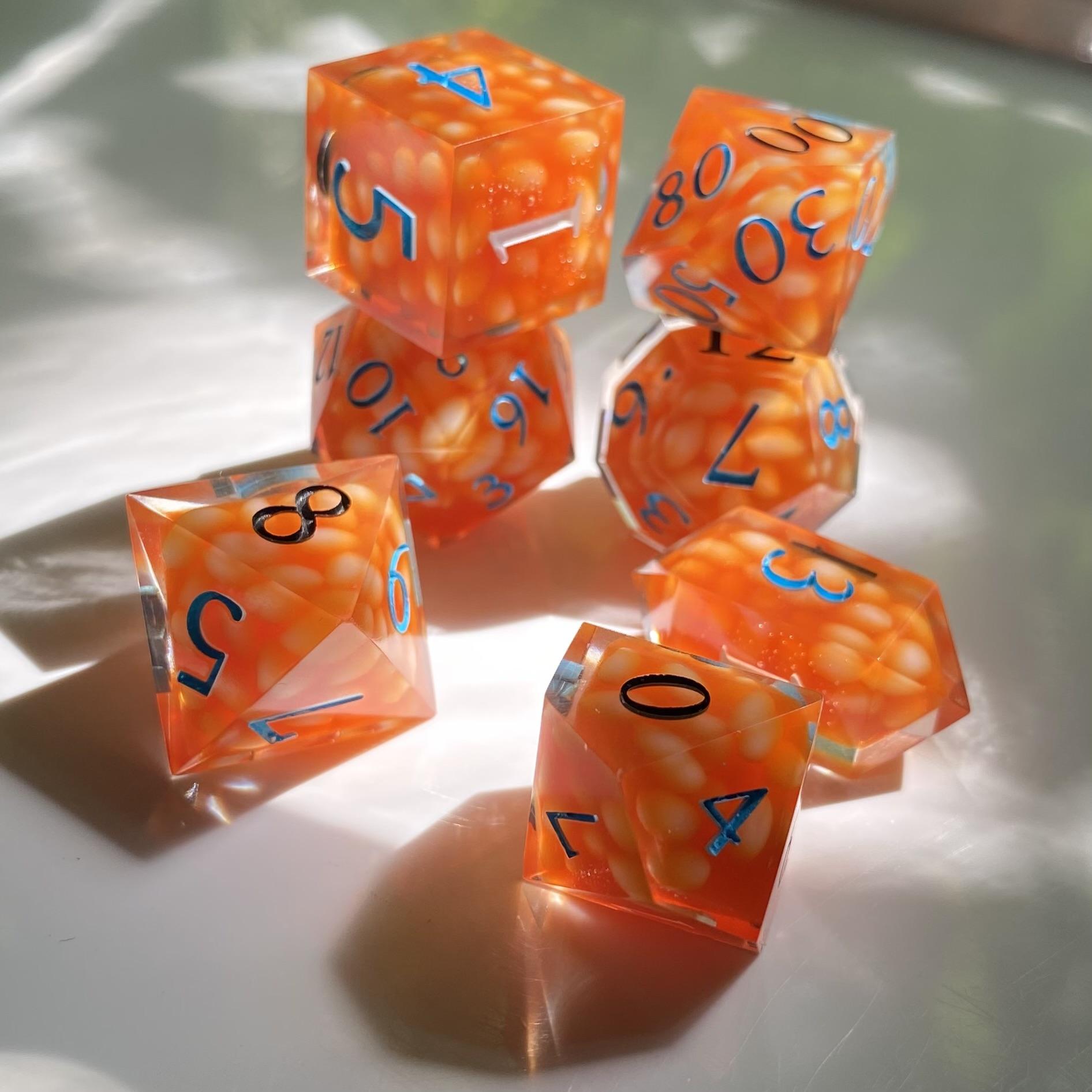 A seven piece gaming set that looks as though each die is filled with canned beans in tomato sauce. The numbers are the colors of a Heinz Beans label: black, white, and aqua blue