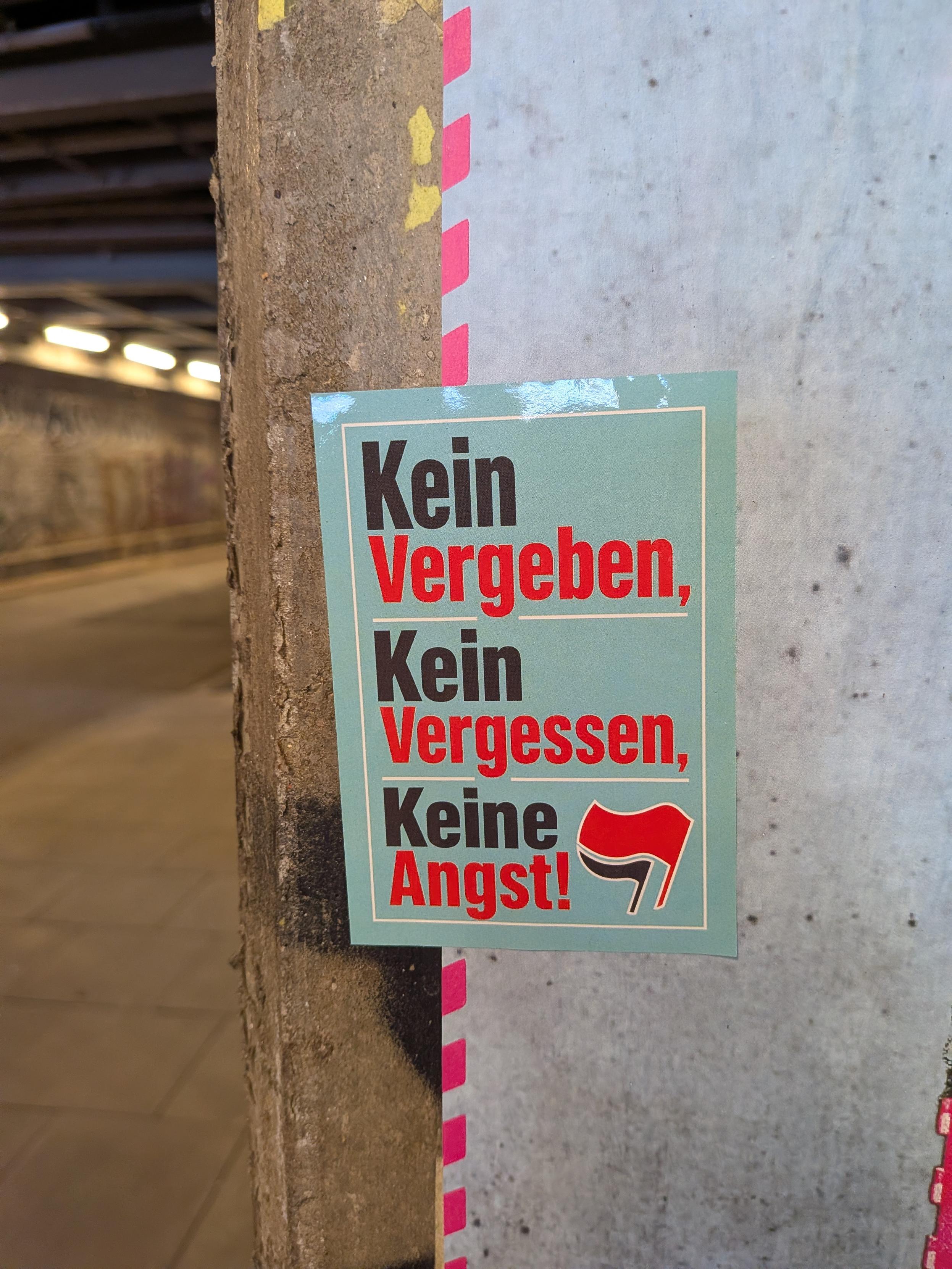 Sticker under a railway underpass: Kein Vergeben, Kein Vergessen, Keine Angst! Translation: No forgiving, No forgetting, No fear! At the bottom, the Antifa logo of the red and black flags appear.