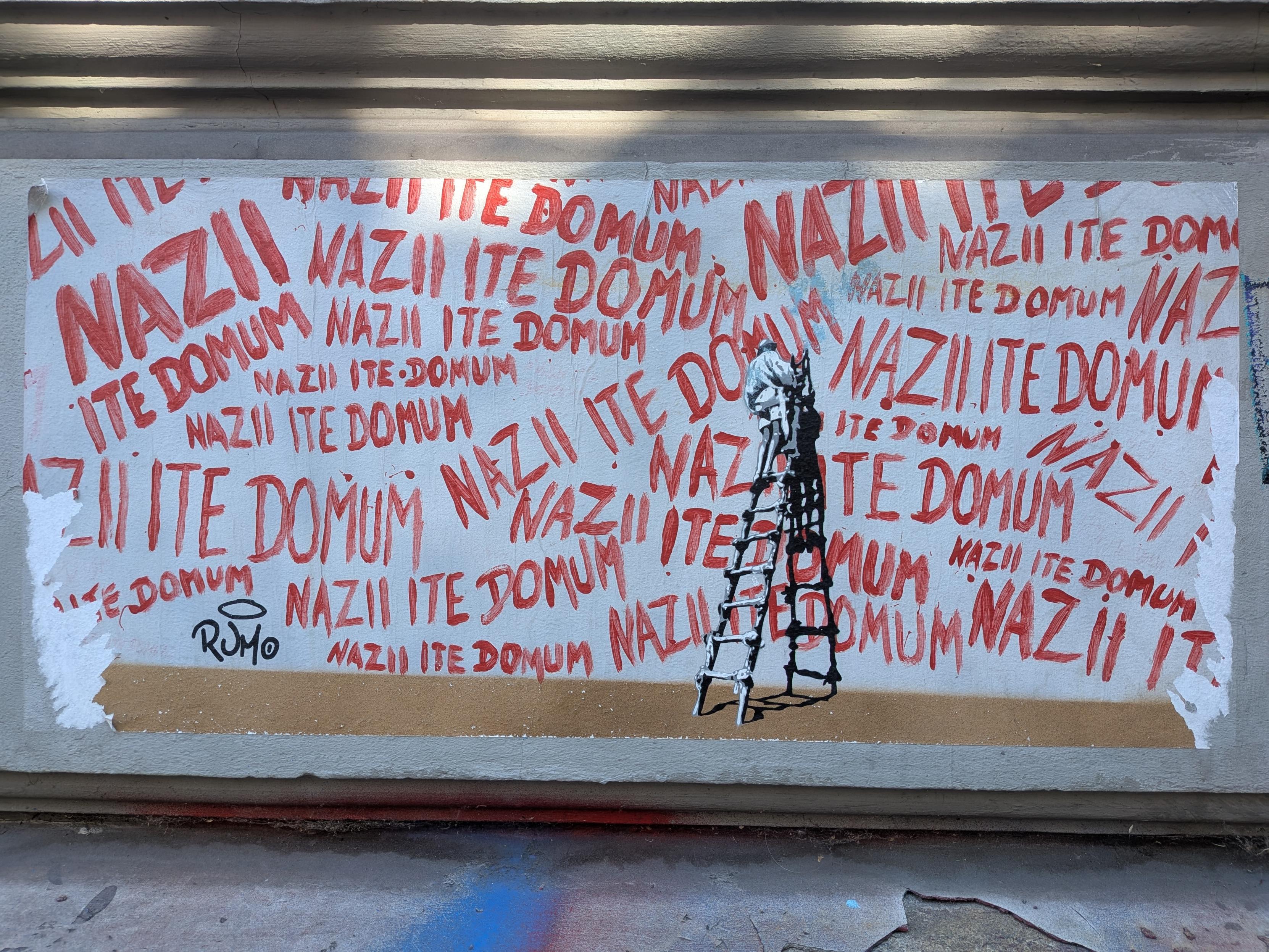 Large "sticker" or maybe just a poster stuck with wallpaper paste - a recreation of the graffiti scene from the Life of Brian film - except instead of hundreds of declarations for the Romans to go home in Latin, it says "Nazii ite domum"