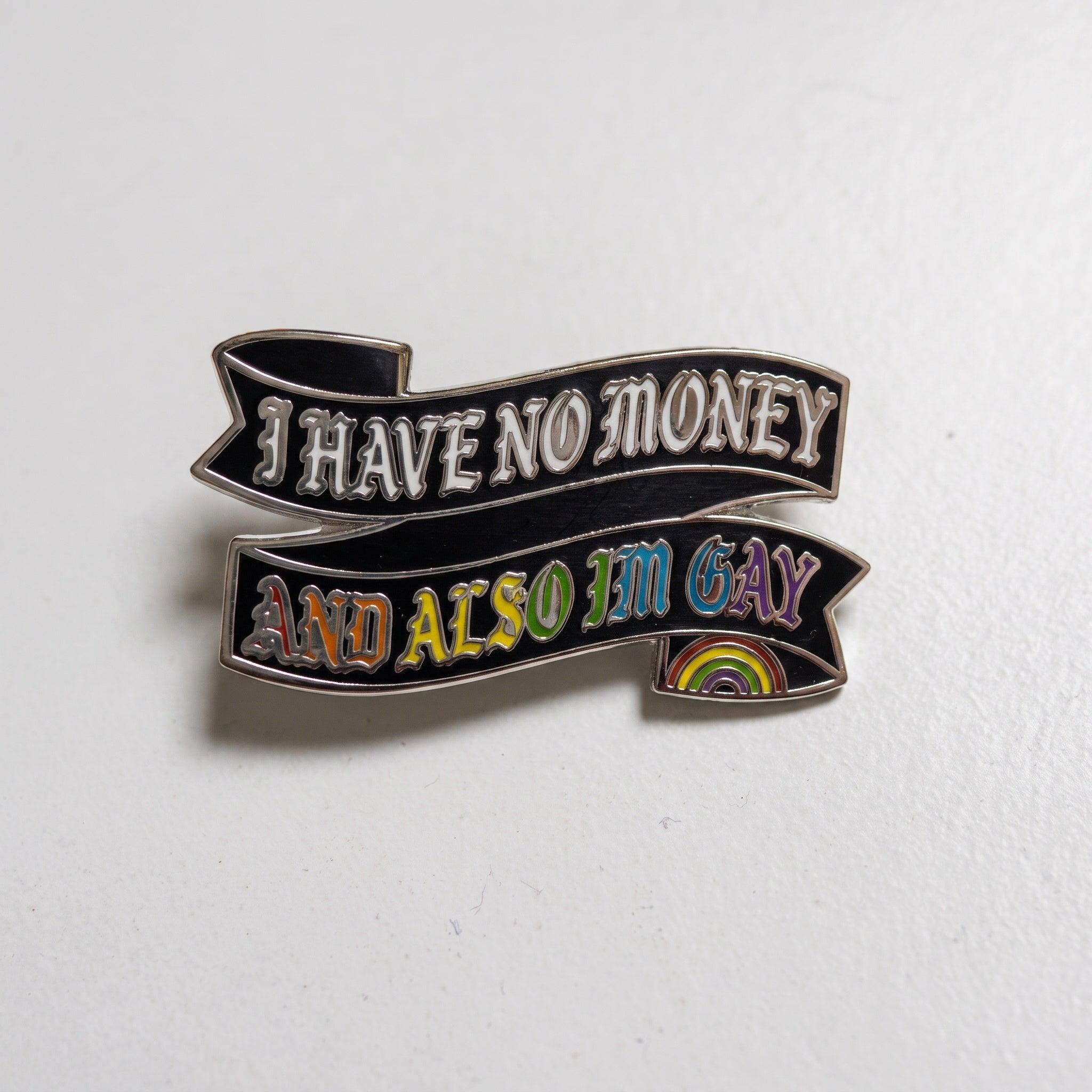Enamel pin shaped like a flowing black banner with silver edges. The text reads "I HAVE NO MONEY AND ALSO I'M GAY" in decorative Gothic-style font, with a small rainbow arch at the bottom right.
