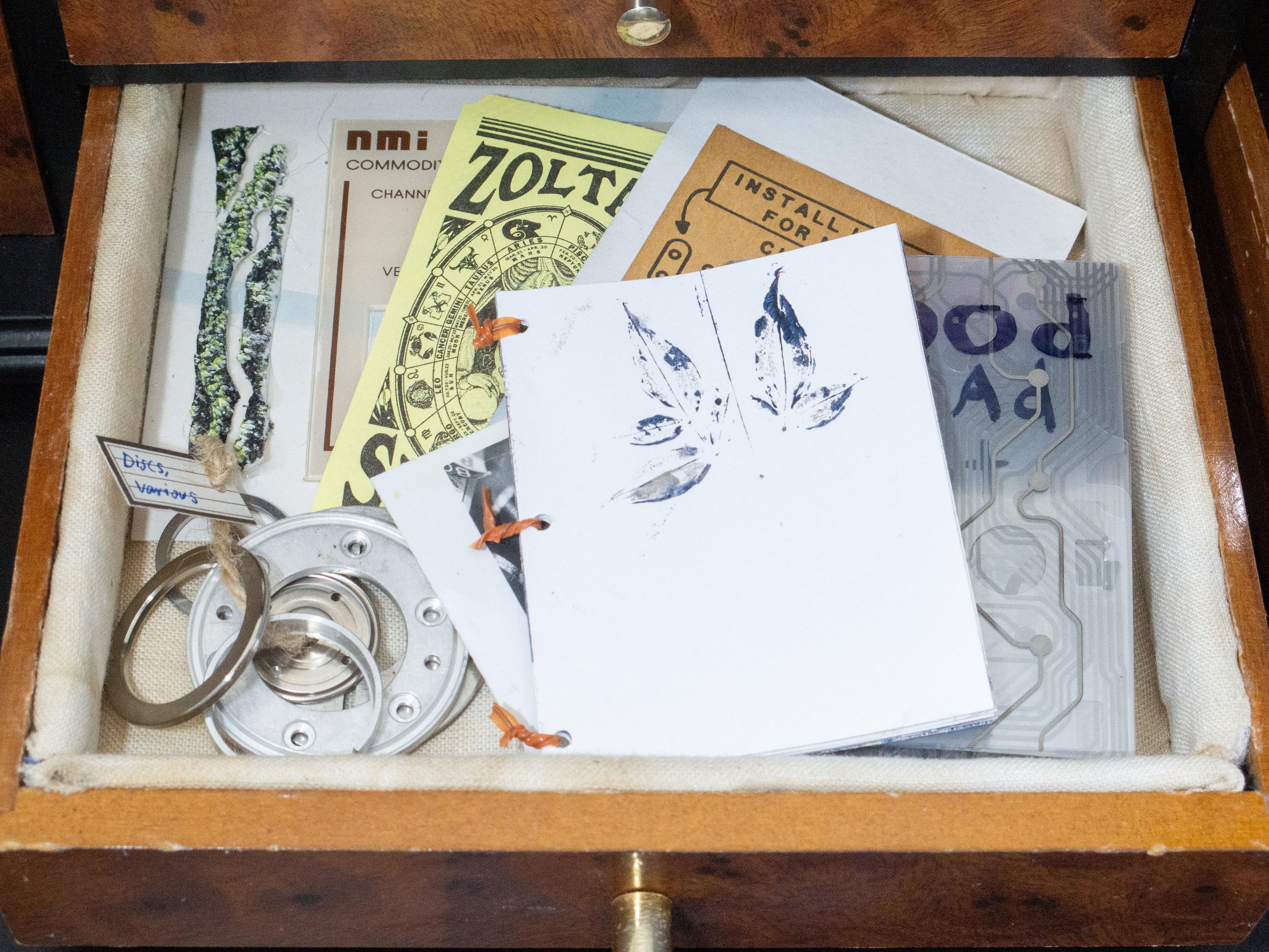 We can more clearly see the paper goods in this image, which also contains a ring of metal rings, labeled "Various," a fortune from Zoltar, a front panel from a commoditator controller, and a zine made of membrane keyboard flexible PCB.