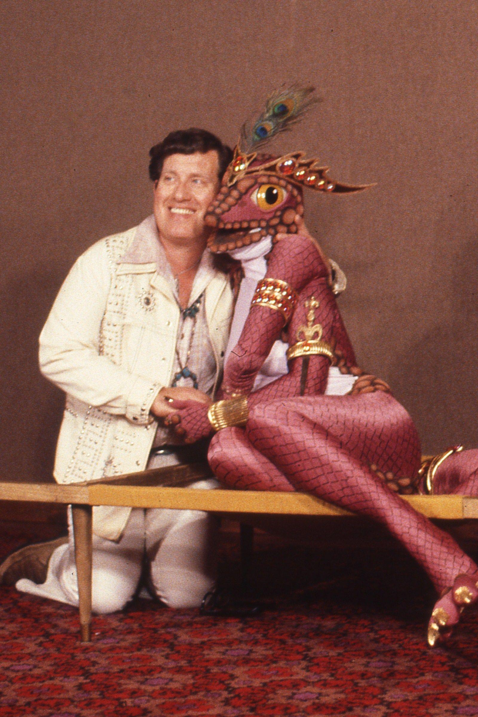 a photo, obviously from the 1970s, of the artist George Barr, posing with like.   I would say "a fursuiter" but it's like, a skintight zentai-ish bodysuit patterned like a lizard's scales, covered in jewelry and with golden claws, and the head is like, sculpted or something, with these gorgeous enormous eyes, but the head is only barely larger than a human's head?  and with some weird alien crown and a peacock feather on top.   I'm in love.