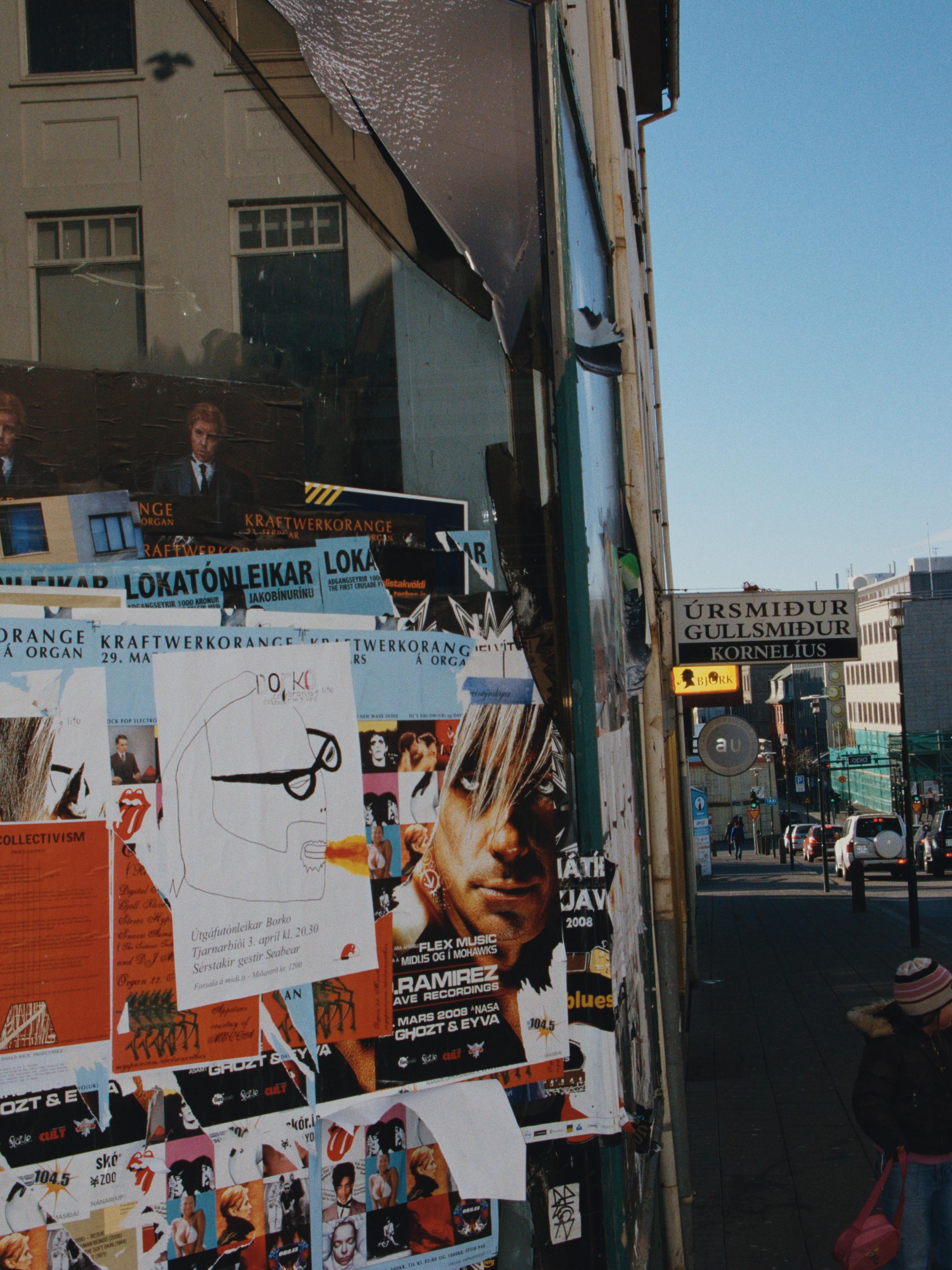 An empty store window is full of flyers. A bit further down the road you can see a sign for a watchmaker and goldsmith and a bit further down there's Austurstræti