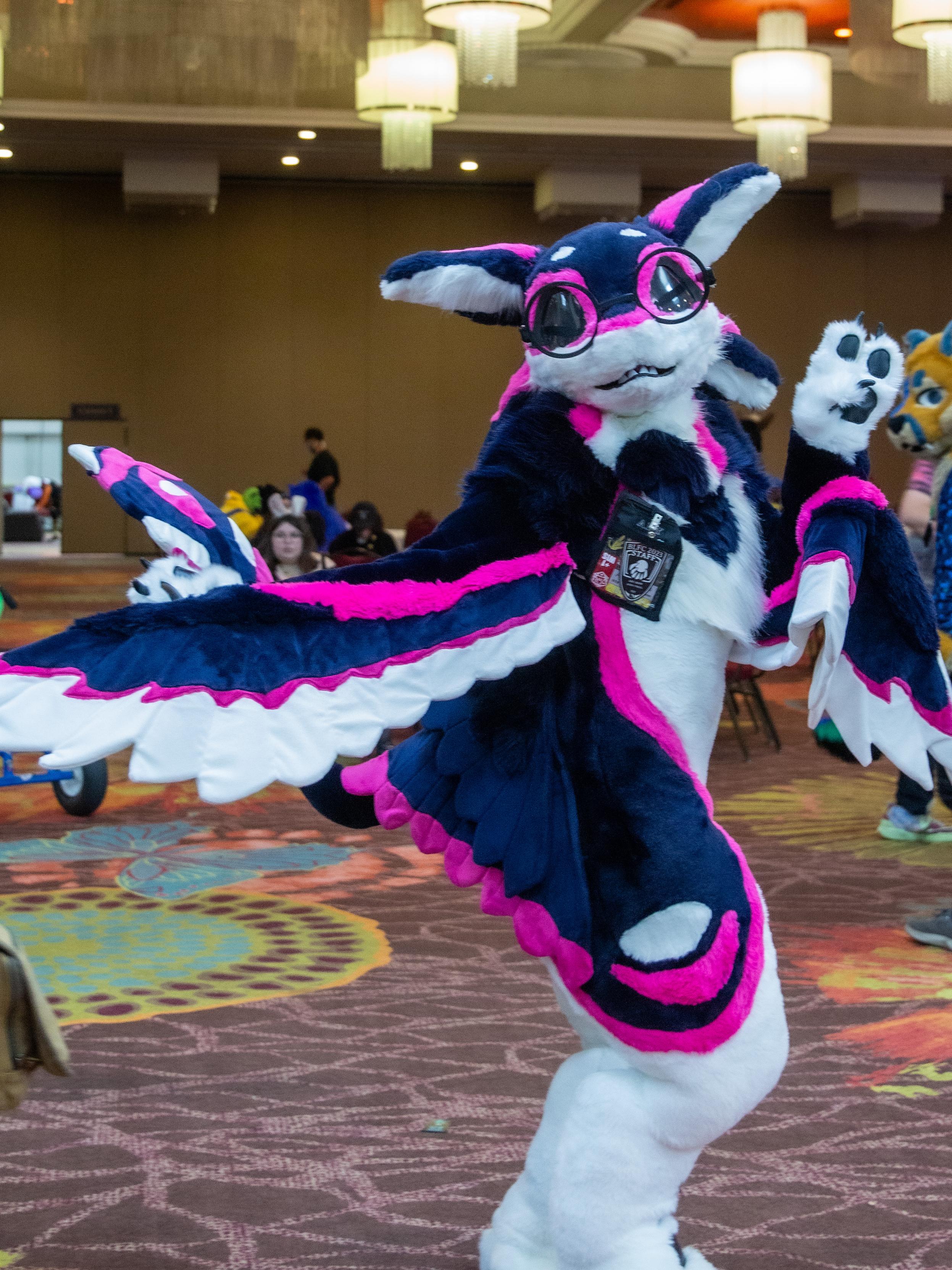An avali fursuiter wearing glasses turning towards the camera showing off.