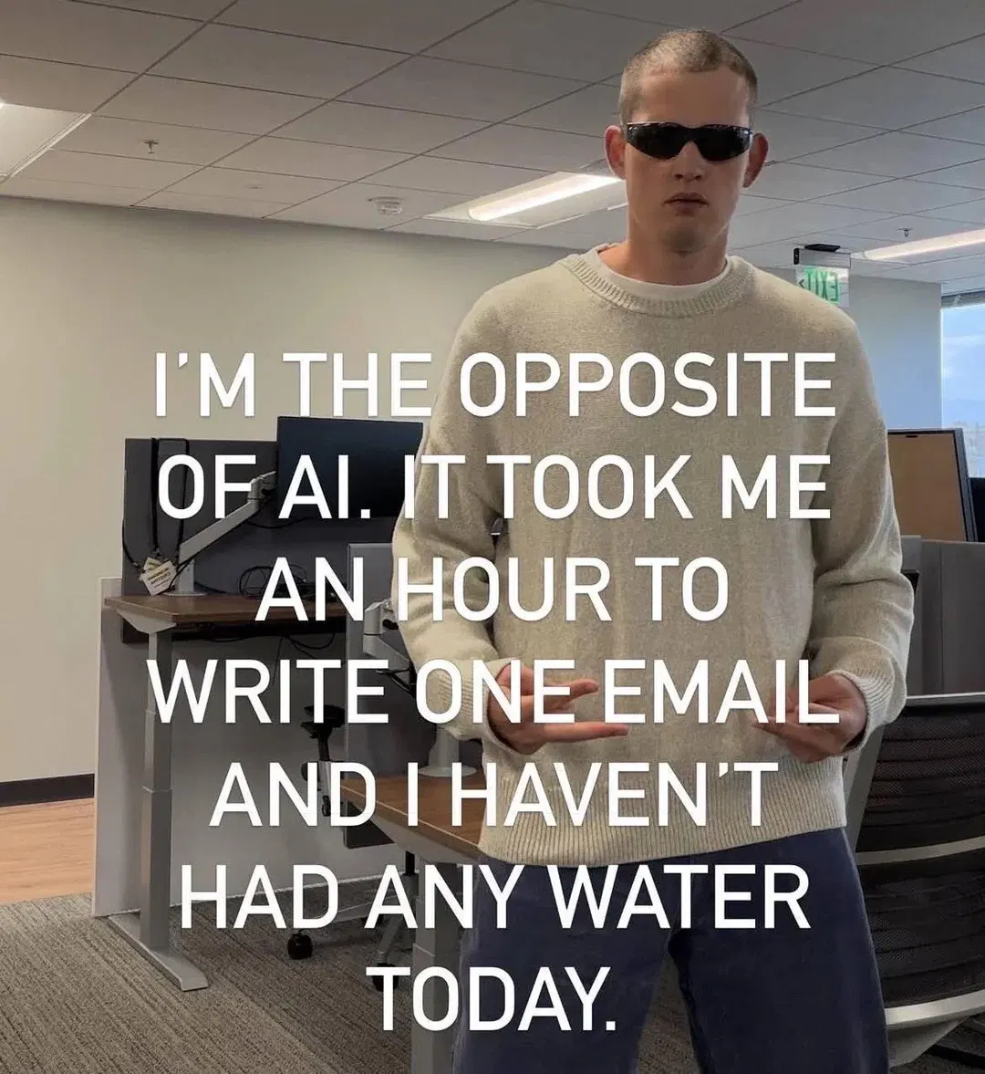 a person wearing sunglasses in an open office environment looking at the viewer captioned "I'M THE OPPOSITE OF AI. IT TOOK ME AN HOUR TO WRITE ONE EMAIL AND I HAVEN'T HAD ANY WATER TODAY."