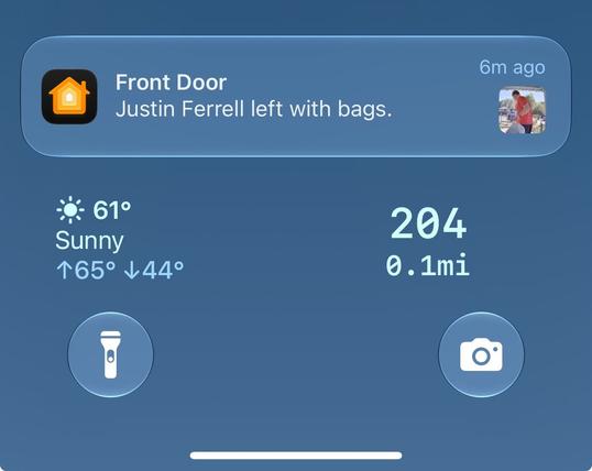 A digital screen shows a notification box with a home icon, displaying the text: "Front Door" and "Justin Ferrell left with bags." The box is on a blue background with a sun icon showing "61°" and "Sunny" with temperatures "↑65° ↓44°." Below, "204" and "0.1mi" are shown. Two circular icons, one with a flashlight and the other with a camera, are on the screen.