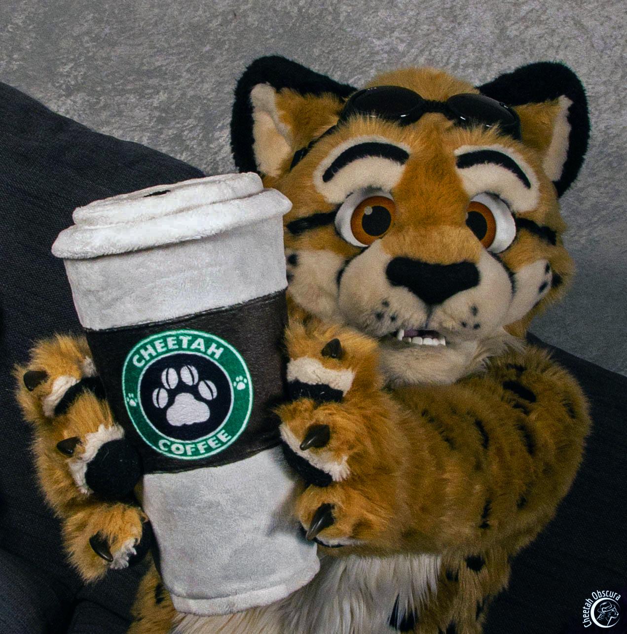 Fursuit photo of Obscura holding out a giant coffee cup with Cheetah Coffee logo on it