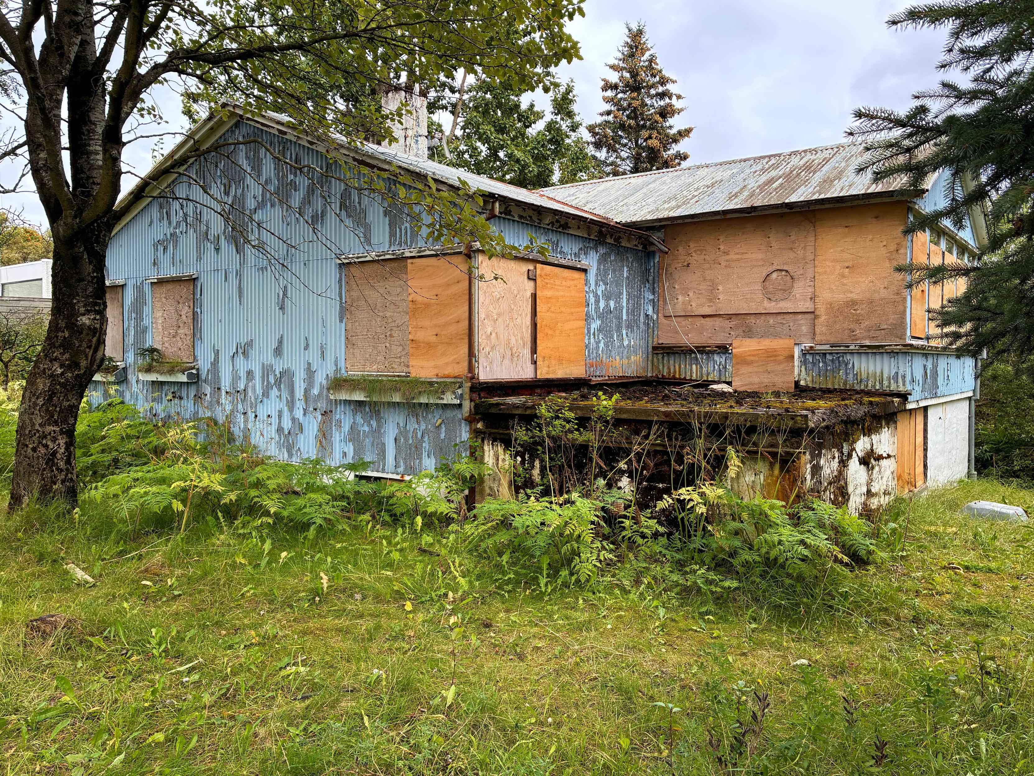 An abandoned blue house in a dilapidated condition surrounded by trees.