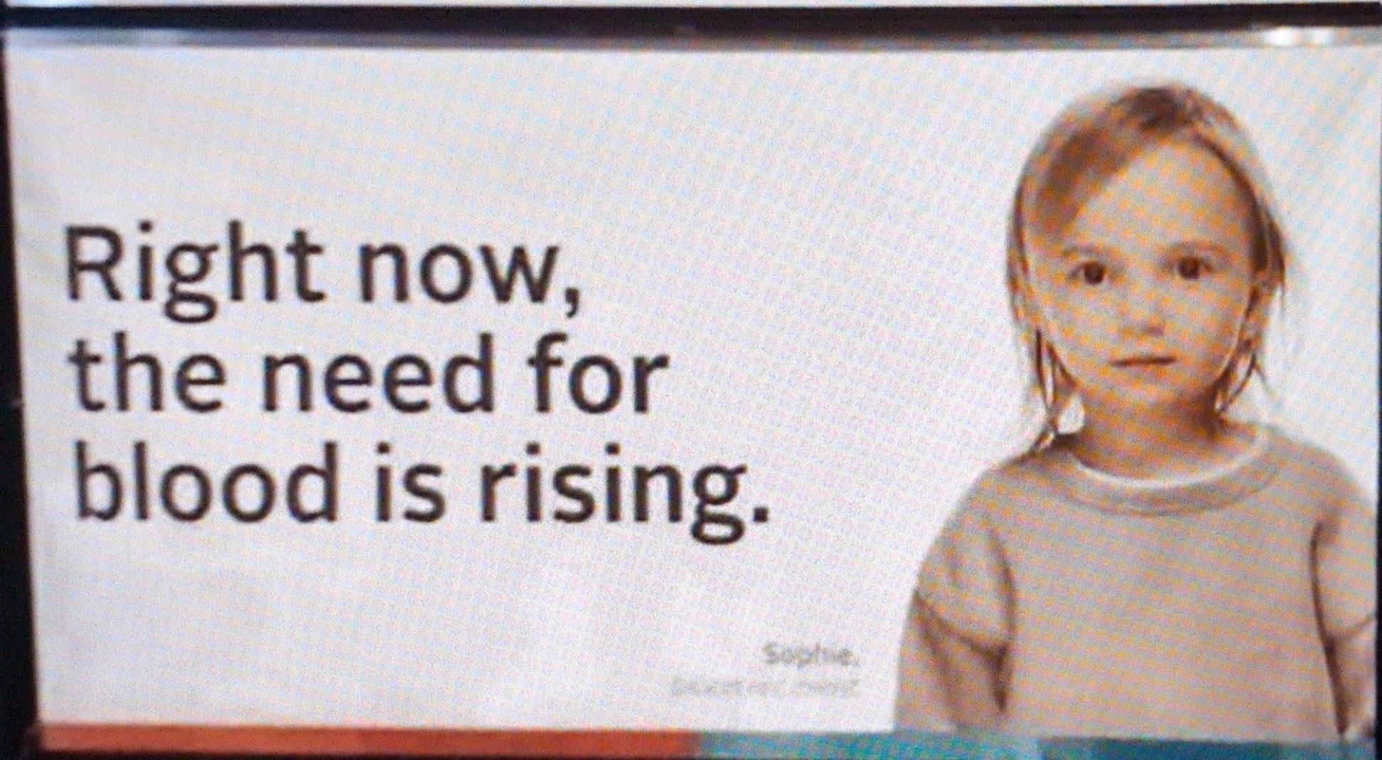 A billboard featuring a blonde child, presumably named Sophie, with the caption "Right now, the need for blood is rising."