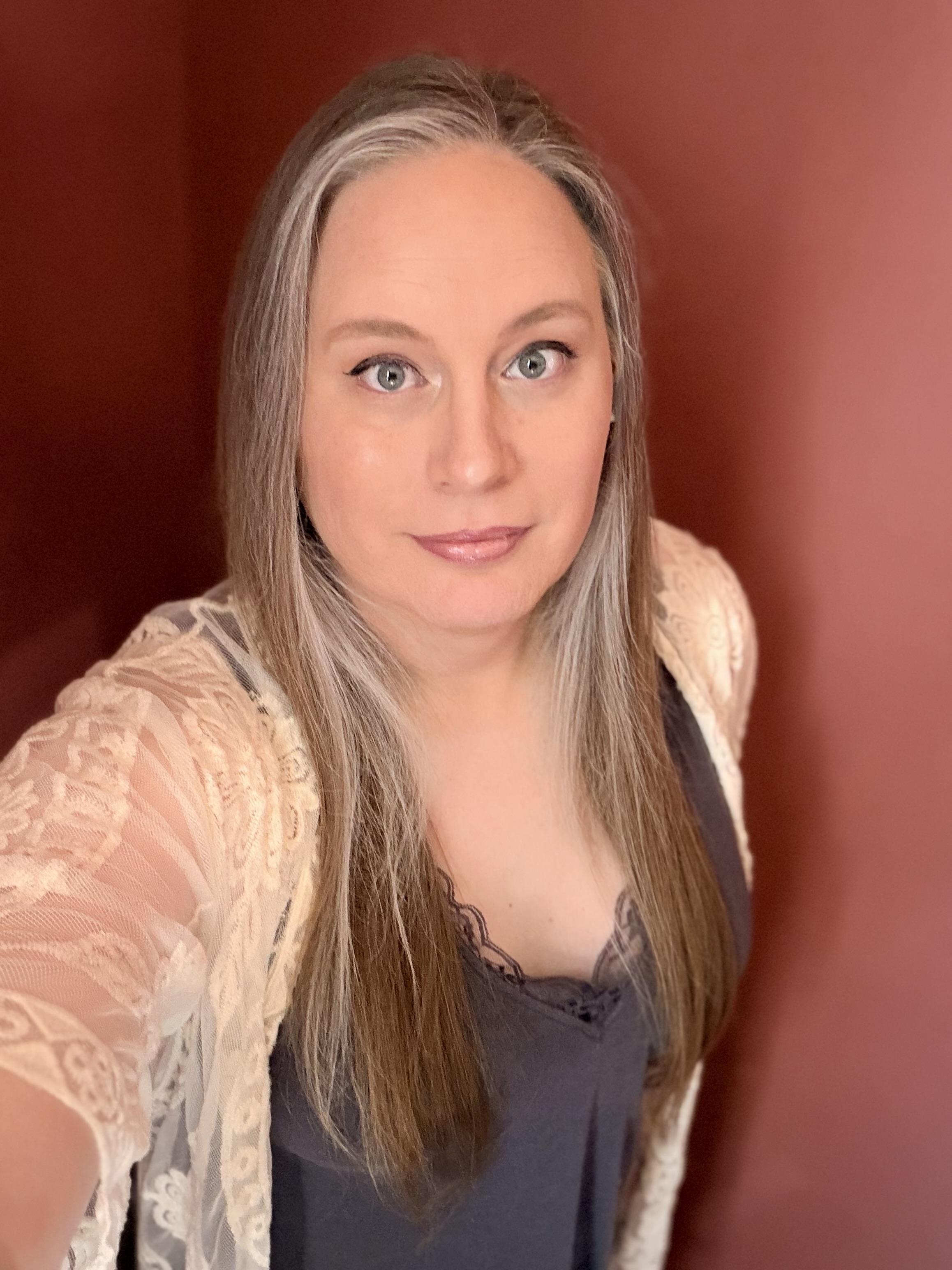 Selfie of a white woman with long blonde & gray hair wearing a dark lacy tank top and a while lacy shawl.