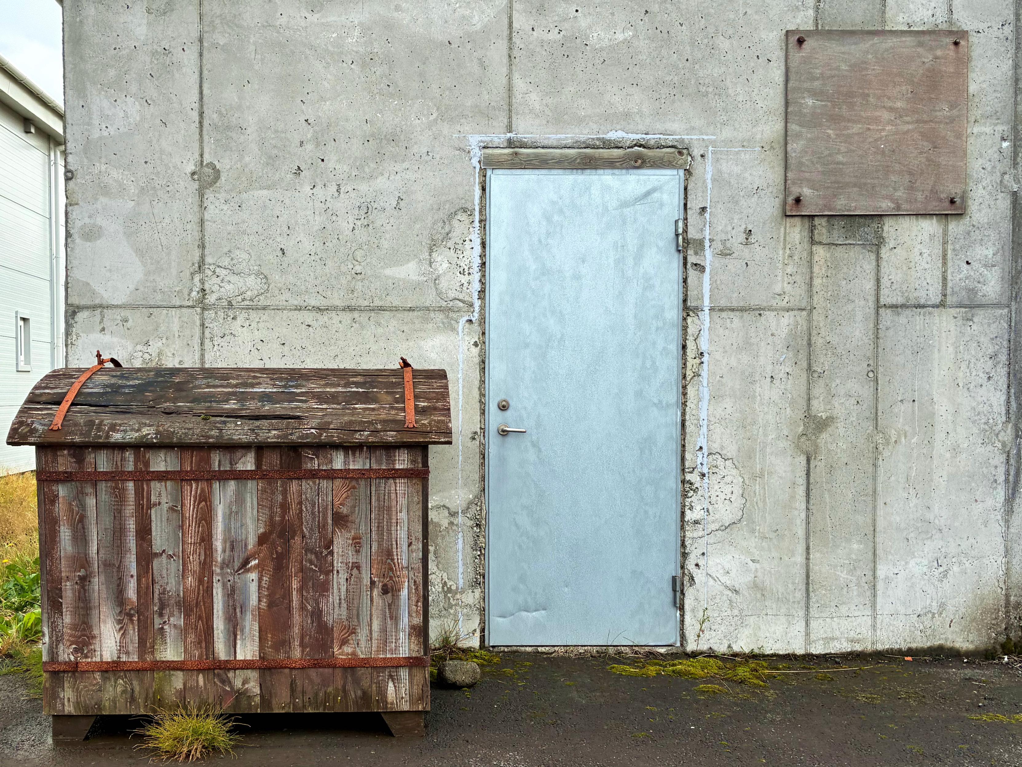 A metal door next to an awesome wooden dumpster.