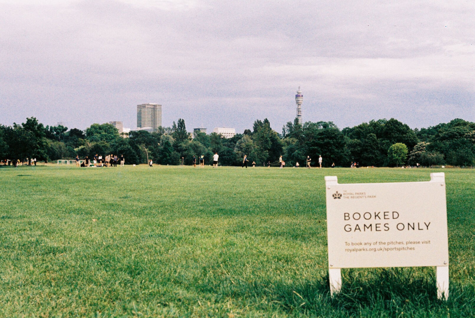 Wide grassy field in The Regent's Park with people playing sports in the distance and a sign reading 'BOOKED GAMES ONLY' in the foreground.