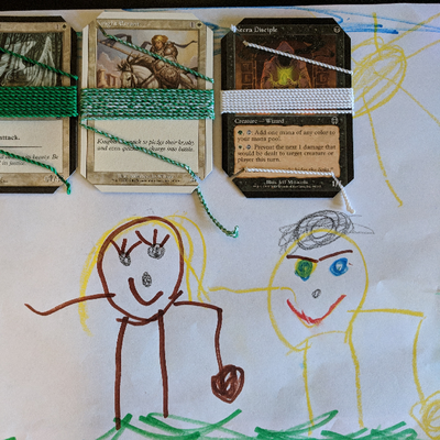 three magic cards with yoyo string wrapped around them: green, white, and mixed. underneath the cards is a child's artwork depicting two people yoyoing.