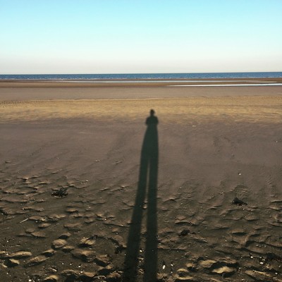 Das Bild zeigt einen Strand mit Schatten einer Person.