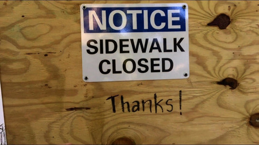 a sign on a plywood wall reading "Notice sidewalk closed" with graffiti under reading "Thanks!"