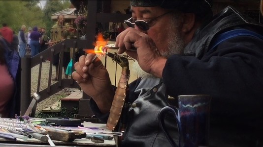 a man sculpts a small glass dragon using a small flame coming out of a brass dragon