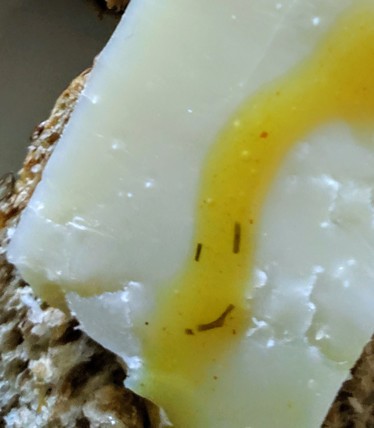 a slice of bread with very matured cheese and a drizzle of honey-mustard sauce in which 3 pieces of dille form a smiling face.