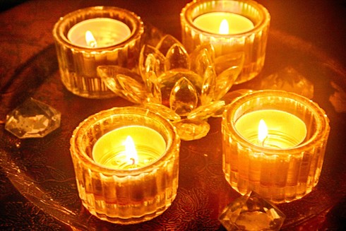 a set of 4 lit tea-lights in glass containers, on a plate with fake crystal decorations.