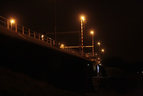 A photograph of the bridge "Buitenhuizerbrug" / "Brug Buitenhuis", over side-channel/Zijkanaal "C" of the Noordzeekanaal (North Sea Canal), taken from below at night so its lights are nicely visible.