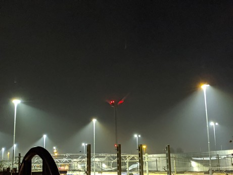 A foggy train yard with a red light illuminating the windmill blades