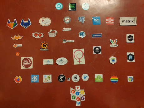 Stickers collected at fosdem 2020 arranged on a floor painted clayish red.