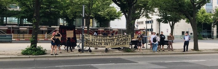 Der Mittelstreifen unter den Linden. Ein paar Menschen mit Bannern, das größte mit Text "No torture, no prison - no repression against Russian antifascists"