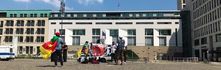 Die französische Botschaft am Pariser Platz, davor ein paar Menschen mit kamerunischen Flaggen und Bannern, auf denen der Rücktritt von Paul Biya gefordert wird.
