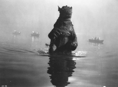 FOTO, monochrome; the Rubber-suit monster Gorgo is wading hip-deep in deep water, with several small-looking Boats nearby in the background.

image, clip from:
https://katmou.files.wordpress.com/2011/11/gorgo_05.jpeg
