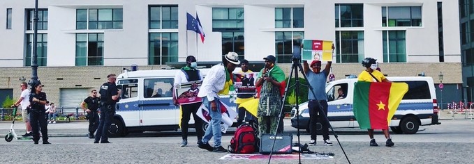 Die französische Botschaft am Pariser Platz, davor Menschen mit Schildern. Einige haben kamerunische Flaggen.