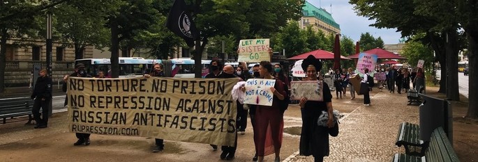 Der Mittelstreifen von Unter Den Linden, darauf protestierende Menschen, links ein Banner "no torture, no prison, no repression against Russian antifascists" rechts Menschen mit Schildern "this is Art, not a Crime", "let my sisters go" und "free yulia tsvetkova"
