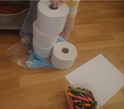 A two-year-old stacking toilet paper rolls on the floor, rather than drawing with his crayons.