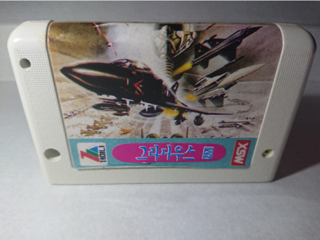 Cart nr 2, likely belonging to box nr 2.
A generic Zemina MSX cartridge with drawings of fighter jets, and a pink sticker label with blue Korean glyphs. On the back was a letratag label "Nemesis 3".