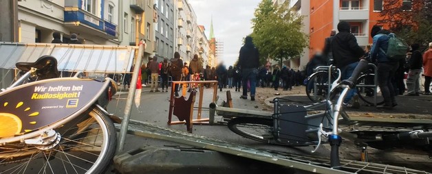 Eine kleine Barrikade aus Zäunen und Leihfahrrädern, im Hintergrund viele Menschen.