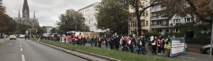 Links im Hintergrund die Kirche am Südstern, im Vordergrund die Straße Hasenheide, darauf viele Menschen mit Bannern und Fahnen.