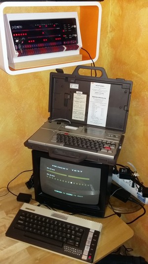 A desk with old computers. An Atari 600XL in front of a TV showing the memory self test. On top of the TV is an Epson HX-20. on a cupboard is a PiDP-11.