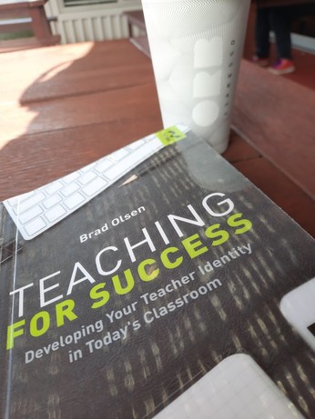 Teaching for Success has a mostly black cover, sitting on a wood table with a white Orb coffee cup in the background.