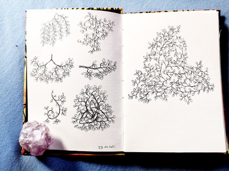 An open sketchbook with 6 small foliage studies on the left page. Bottom right is foliage on a triskel. On the right page is a triskel indicated by the branches of foliage. 