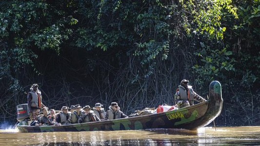 Pirogue militaire de 10 personnes longeant la rive.
Eau du fleuve en premier plan, forêt derrière.