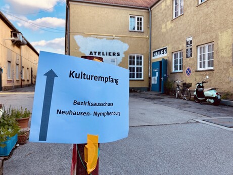 Hinweisschild "Kulturempfang" im Vordergrund vor grüngelben Häuserwänden des Kreativlabors München.