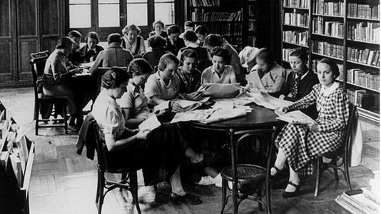 Mujeres leyendo y escribiendo alrededor de dos mesas en la biblioteca de la Residencia de Señoritas de Madrid.
