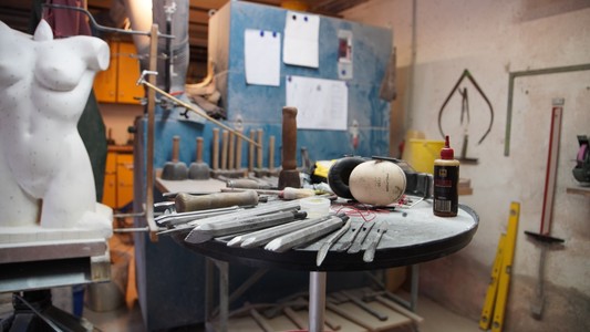 Bildhauer Werkstatt in Reichelsheim im Odenwald. Das Handwerkzeug im Vordergrund hat der Bildhauer Markus Eck für seine Arbeit an der Statur links im Bild genutzt. Im Hintergrund sind die Zeichnungen von Markus Eck zu sehen. 