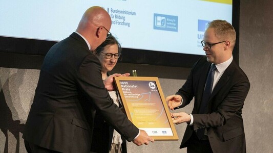 Johannes Orphal (links), Beauftragter des Präsidiums für Klimaschutz und Nachhaltigkeit, und Senja Post, wissenschaftliche Leiterin des ZAK, nehmen den „Nationalen Preis – Bildung für nachhaltige Entwicklung“ von Staatssekretär Jens Brandenburg entgegen.