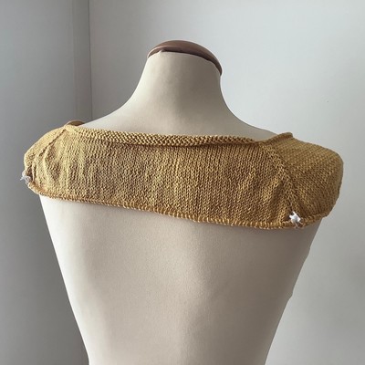 The start of knitted tee in golden yellow yarn, shown from the back on a mannequin 