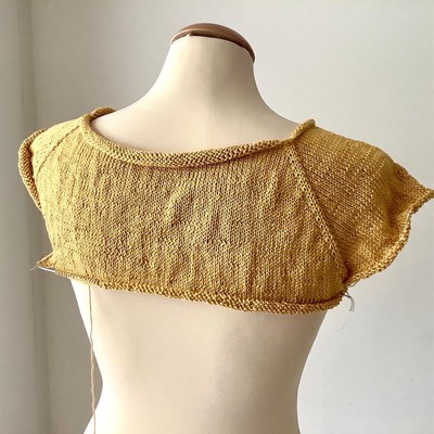 Knitted yellow tee, partially done, shown from the back on a mannequin 