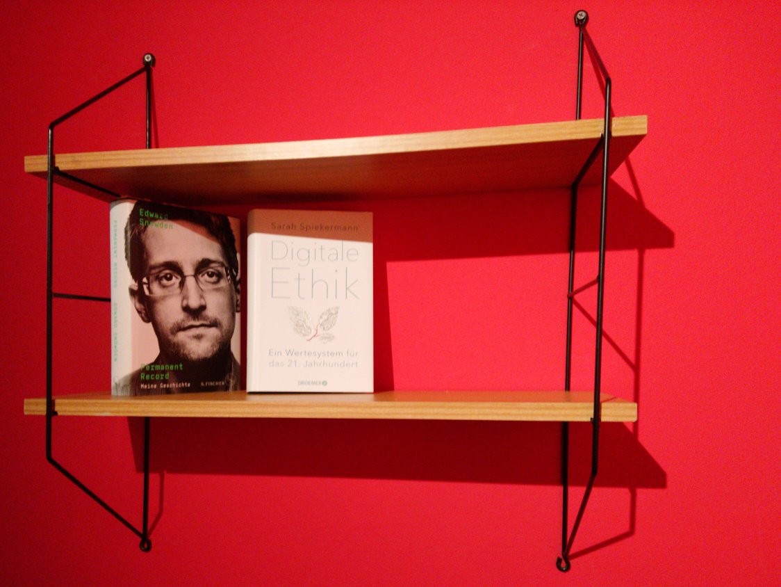 Eine rote Wand mit einem kleinen hänge Bücherregal. Es sind zwei Bücher zu sehen und noch viel Platz.