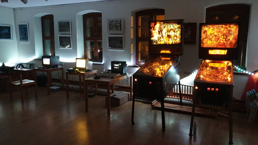 A row of three retro computers and two pinball machines in an illuminated room.
From right side, white light.