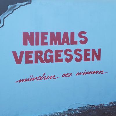Auf einer weiß gesprühten Betonwand in leuchtend pinken Lettern:
NIEMALS
VERGESSEN
münchen oez erinnern
